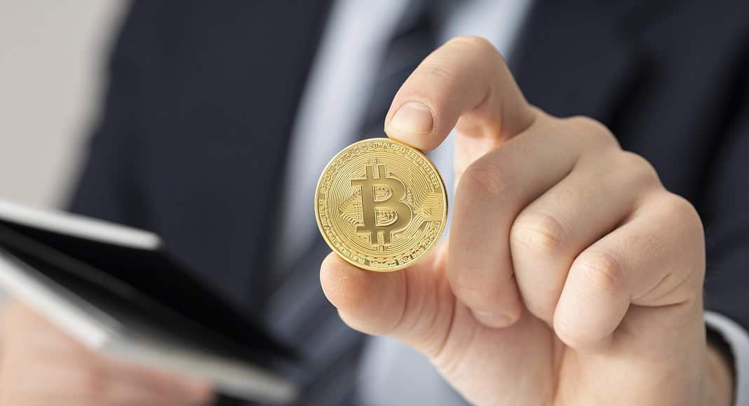 Una persona in giacca e cravatta tiene con sicurezza una moneta Bitcoin fisica tra le dita, a simboleggiare la fusione della finanza tradizionale con il mondo all'avanguardia della valuta digitale.