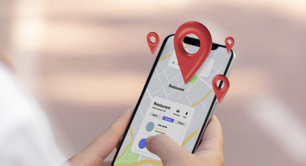 Una persona tiene in mano uno smartphone che mostra Google Maps con più puntine di posizione. Lo sfondo mostra un sentiero all'aperto.