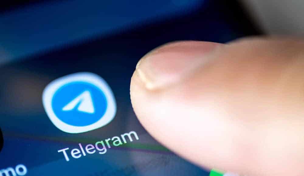 Un dito tocca con entusiasmo l'icona familiare dell'app Telegram, dando vita all'elegante piattaforma sullo schermo dello smartphone.