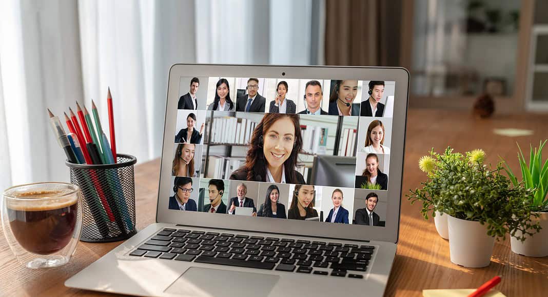 Un laptop sul tavolo mostra una videoconferenza Zoom con più persone. Nelle vicinanze, una tazza di caffè, matite e una pianta aggiungono un tocco di comfort all'ambiente.