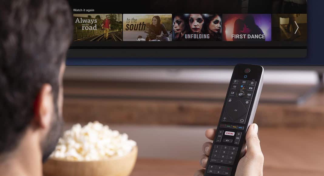 Una persona è sdraiata sul divano, con il telecomando in mano, immersa nella visione di Netflix, mentre una ciotola di popcorn è invitantemente appoggiata sul tavolo.