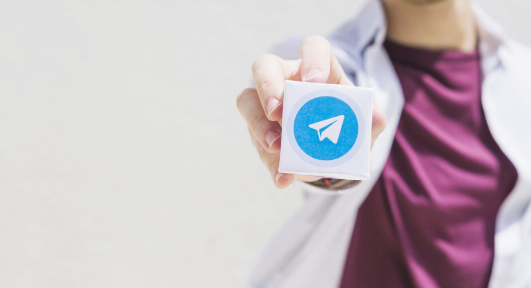 Una persona tiene in mano un cubo con il logo di Telegram, che spicca su uno sfondo semplice.