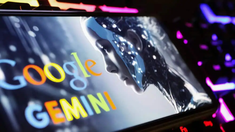 Lo schermo di uno smartphone mostra Google Gemini, una figura futuristica simile a un essere umano, su uno sfondo con una tastiera dai colori vivaci.