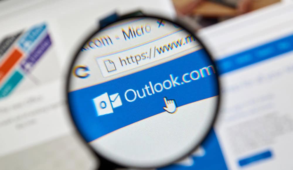 Una lente di ingrandimento si concentra sulla pagina web di Outlook.com all'interno di un browser, evidenziandone il logo e l'URL, un po' come se si sbirciasse attraverso una finestra digitale in Windows Mail.