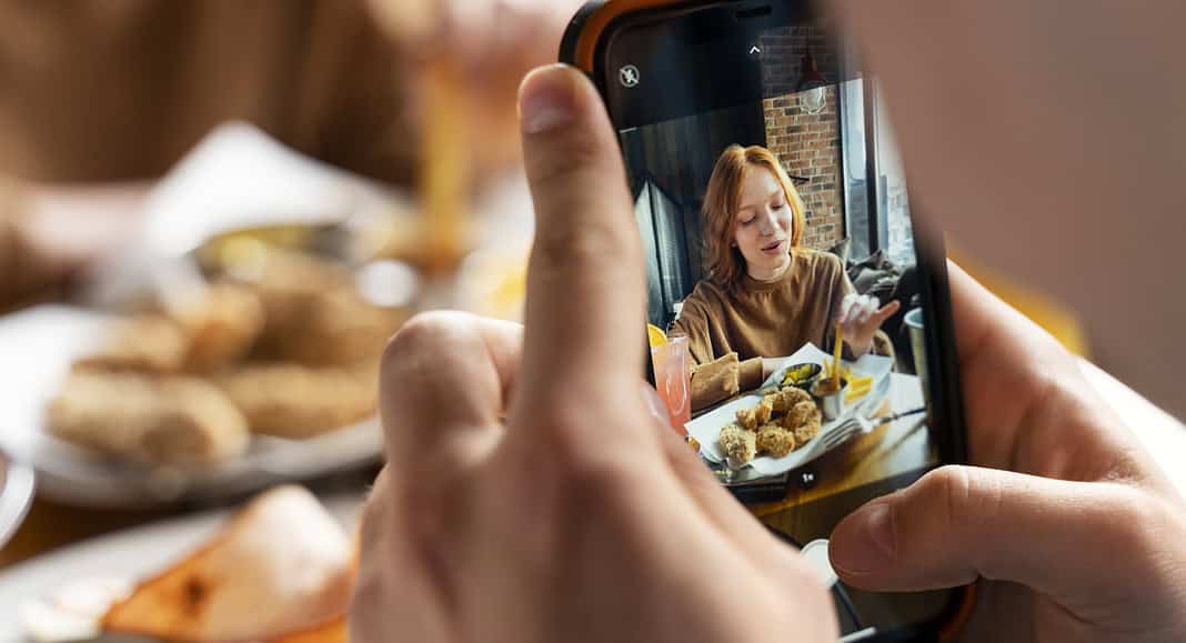 Una persona scatta una foto su WhatsApp a qualcuno che sta gustando un pasto in un ristorante, immortalando perfettamente sia il piatto delizioso sia il commensale in un unico fotogramma.