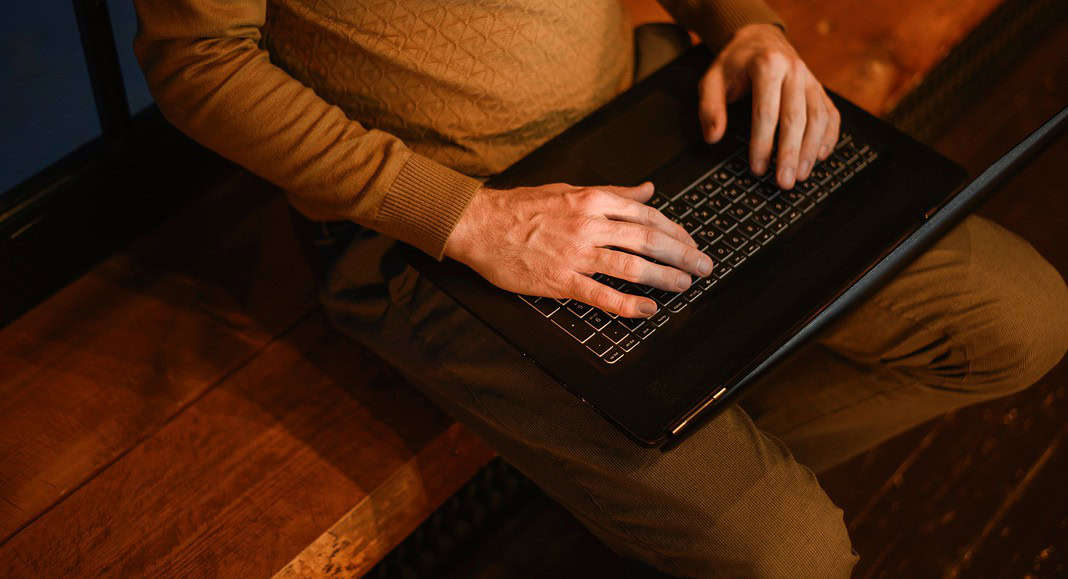 Una persona sta scrivendo su un computer portatile, interagendo con ChatGPT, mentre è comodamente seduta su una panca di legno al chiuso.